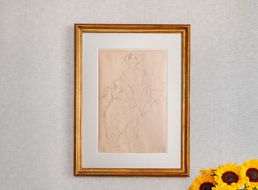 Gerahmte Bleistiftskizze einer sitzenden Person auf beigem Papier, die auf einer hellen, strukturierten Wand mit Sonnenblumen in der rechten unteren Ecke dargestellt ist.